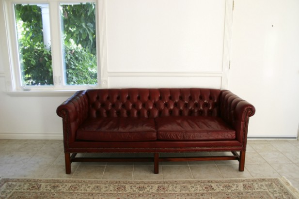 Foto de um sofá vermelho com paredes brancas e uma janela.